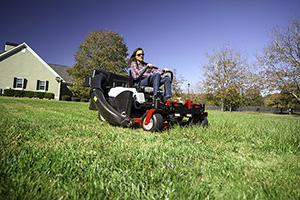 woman on a big riding mower runs across her yard picking up leaves and other debris to get her lawn ready for winter