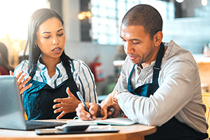 two persons of color working at the business they own go over documents and figures prepping for their home mortgage application