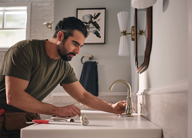 guy stares intently at a kitchen sink faucet, tools nearby, planning many DIY project to replace the faucet