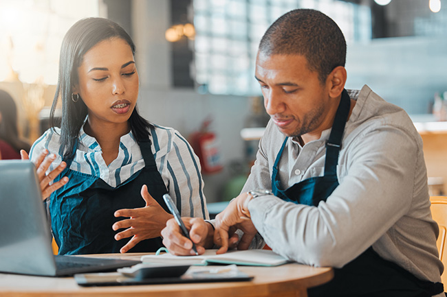 two persons of color working at the business they own go over documents and figures prepping for their home mortgage application