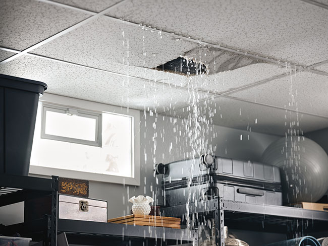 view of the ceiling of a home with water pouring through ceiling tiles caused by a water leak