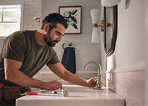 guy stares intently at a kitchen sink faucet, tools nearby, planning DIY project to replace the faucet